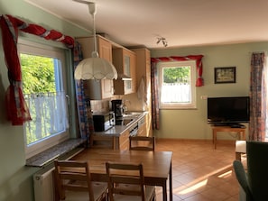 A compact kitchen with a dining area, a TV, and a window with curtains.