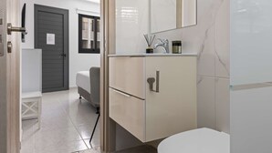 Une salle de bain moderne avec un lavabo en marbre, un grand miroir et une porte grise.