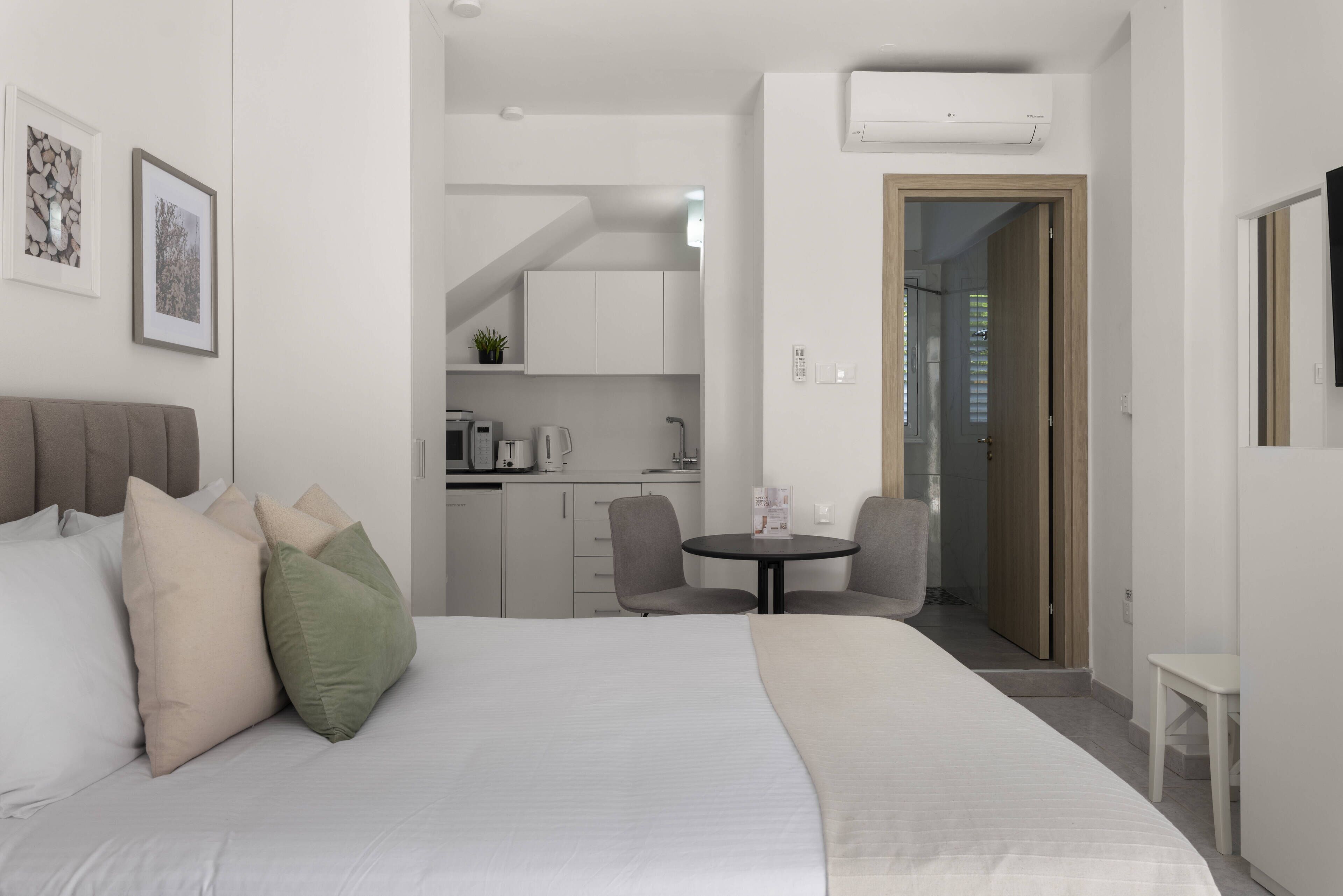 A modern hotel room with a large bed, a small kitchen area, and a dining table.