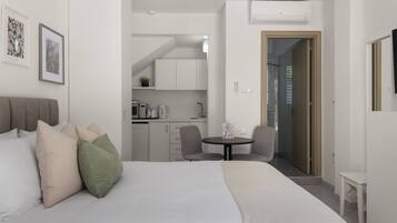 A modern hotel room with a large bed, a small kitchen area, and a dining table.