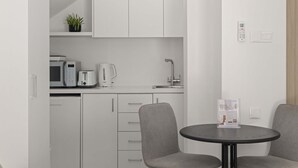 Une cuisine moderne avec des meubles blancs, un four à micro-ondes, un grille-pain et une bouilloire. On y trouve une petite table avec deux chaises et un panneau posé dessus.