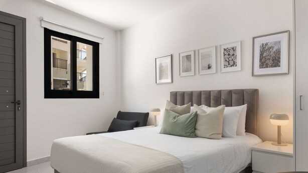 Une chambre à coucher avec un grand lit, une table de chevet avec une lampe, une chaise et une fenêtre avec des stores.