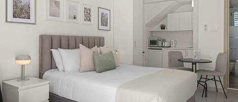 Ein modernes Schlafzimmer mit einem Bett, Nachttischen, einem Schreibtisch und einer kleinen Küchenzeile.