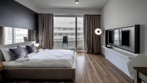 Ein modernes Hotelzimmer mit einem großen Bett, einem Flachbildfernseher, einem Schreibtisch und einem Balkon mit einem Sessel.