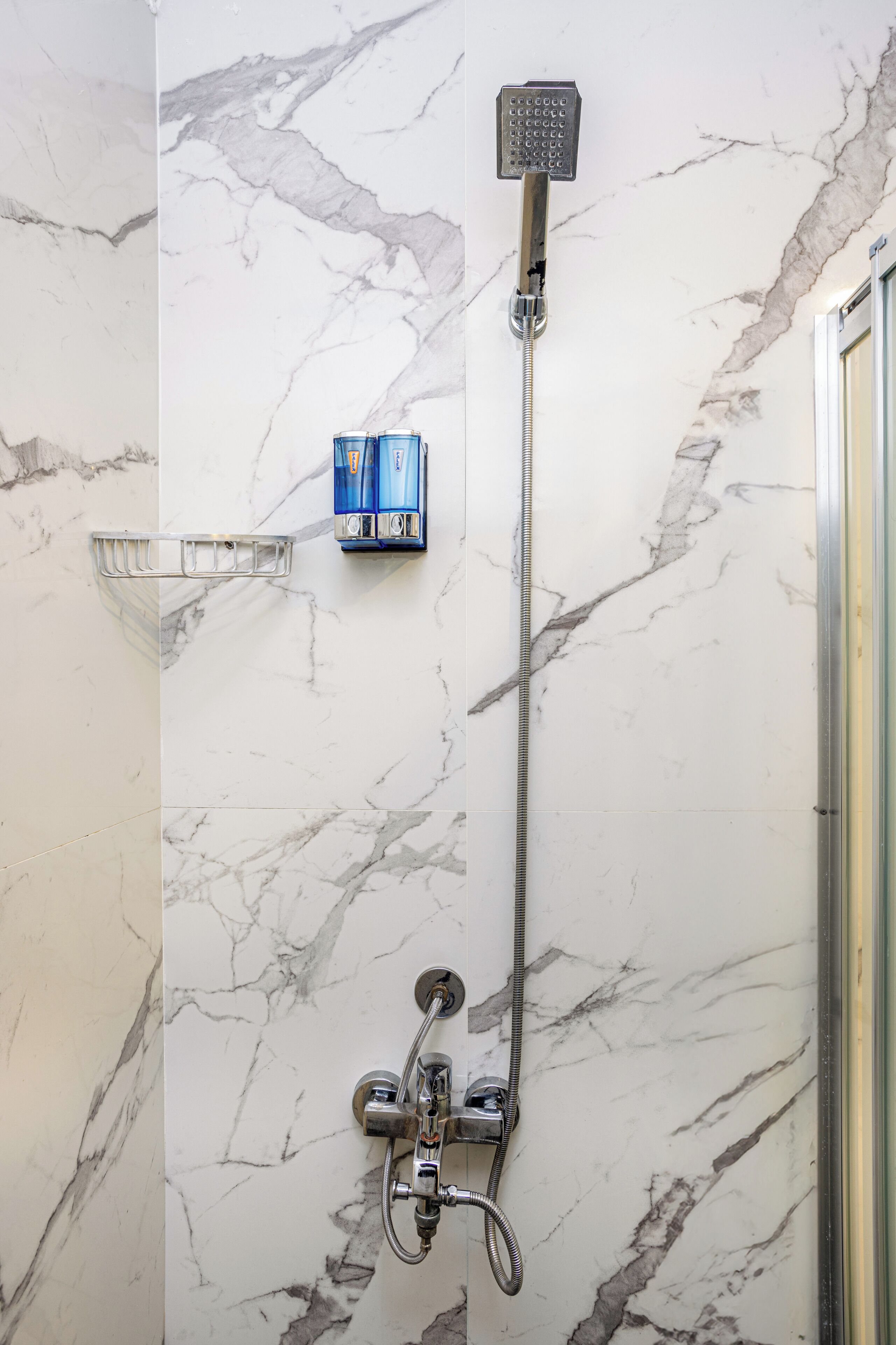 A bathroom with a shower, a towel rack, and a soap dispenser.