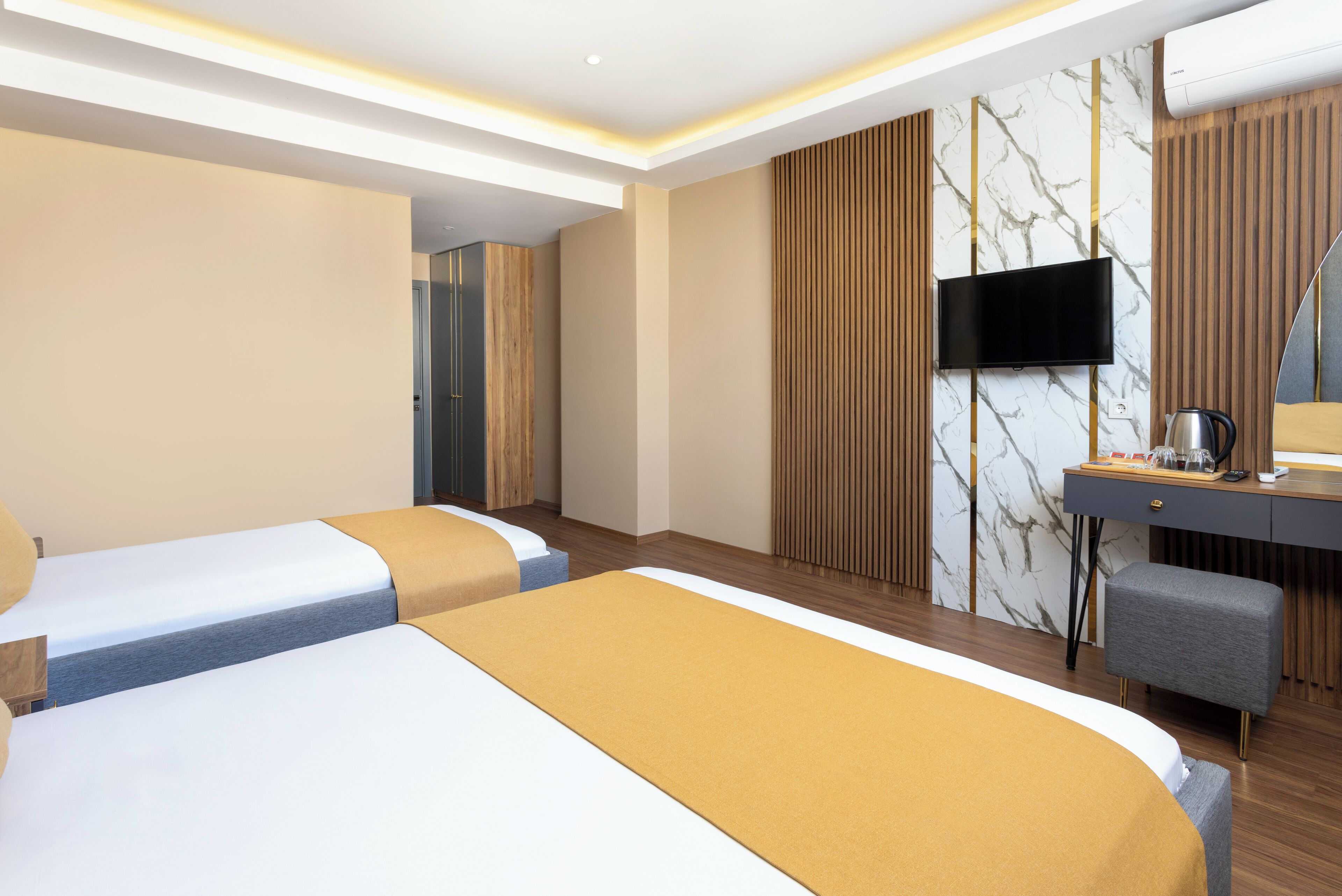 Une chambre d’hôtel avec deux lits, un bureau, une chaise, une télévision et un mur décoré d’un motif imitant le marbre.