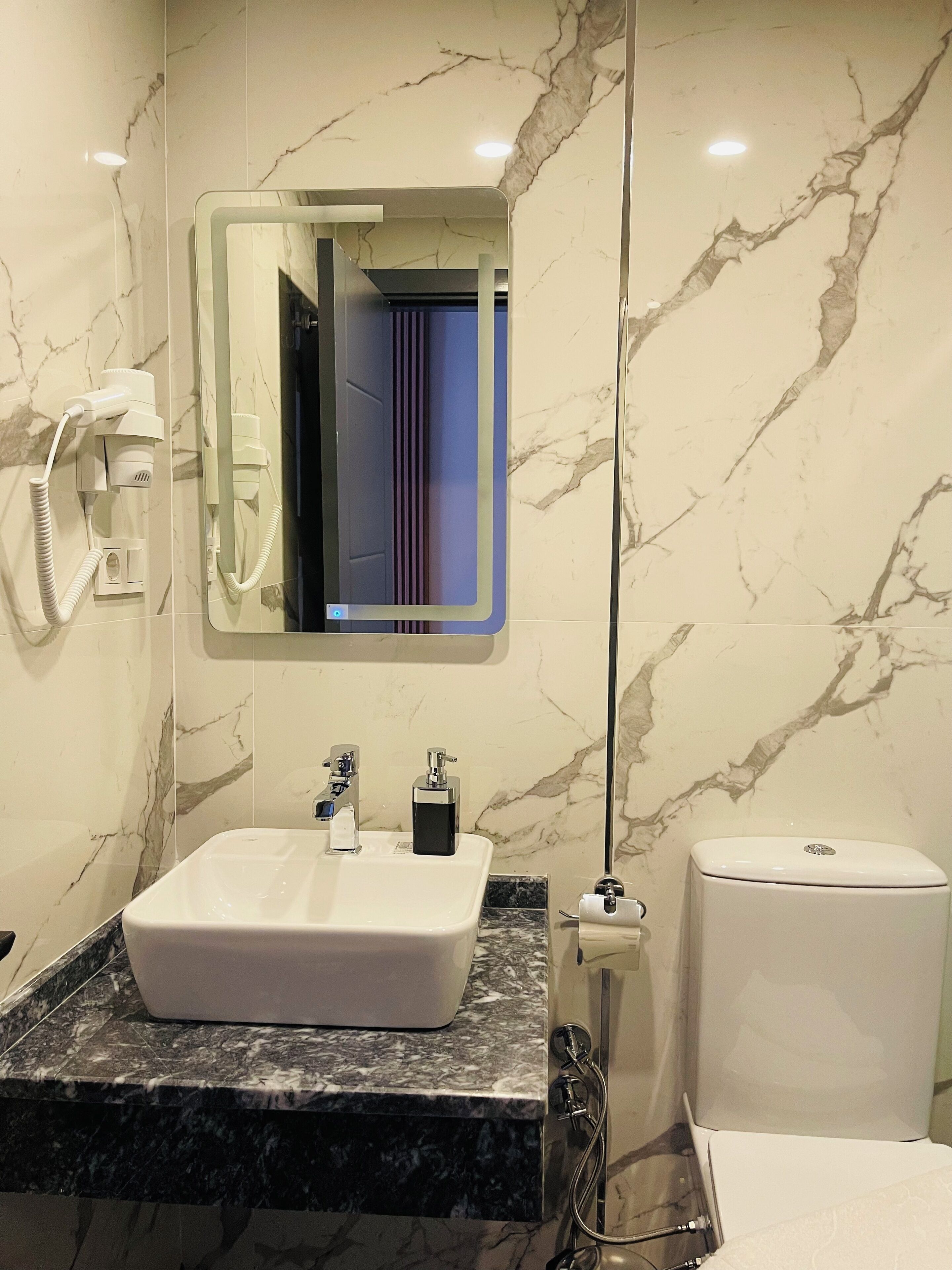 A bathroom with a white sink, a mirror, a toilet, and a hairdryer on the wall.
