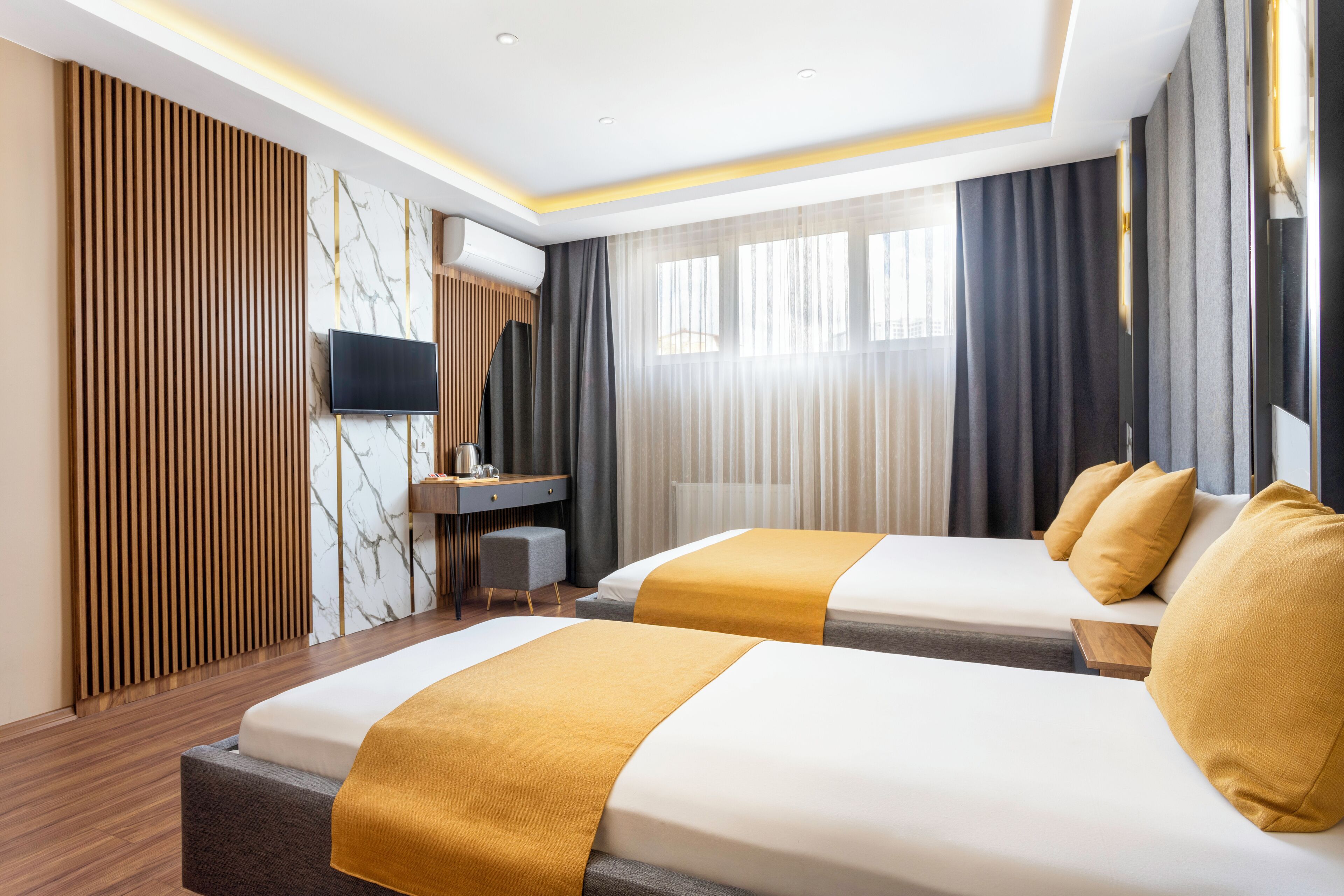A hotel room with two beds, a desk, a TV, and a large window with curtains.