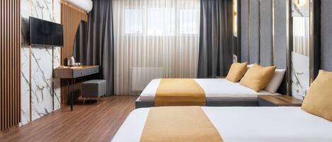 A hotel room with two beds, a TV, a desk, and a large window with curtains.