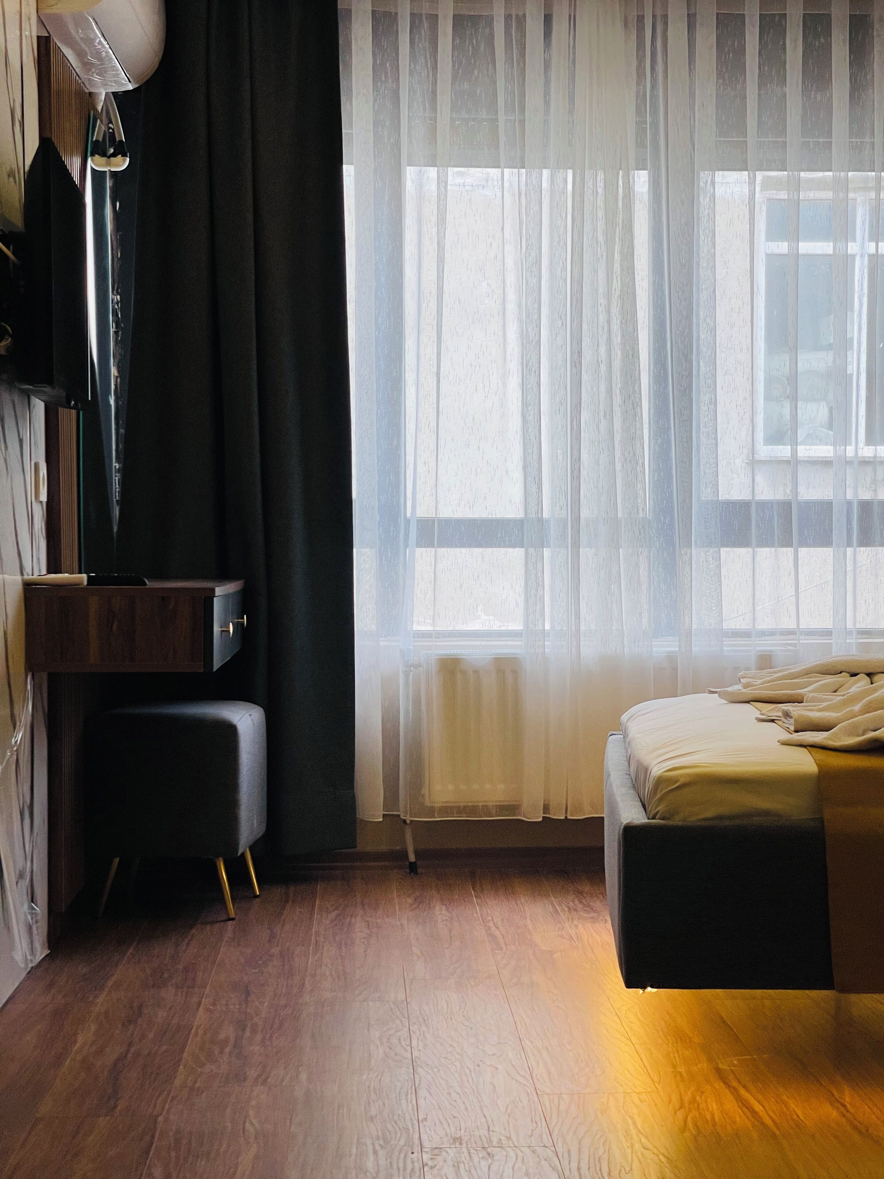 A bedroom with a bed, a desk, a chair, a lamp, and a window with sheer curtains.
