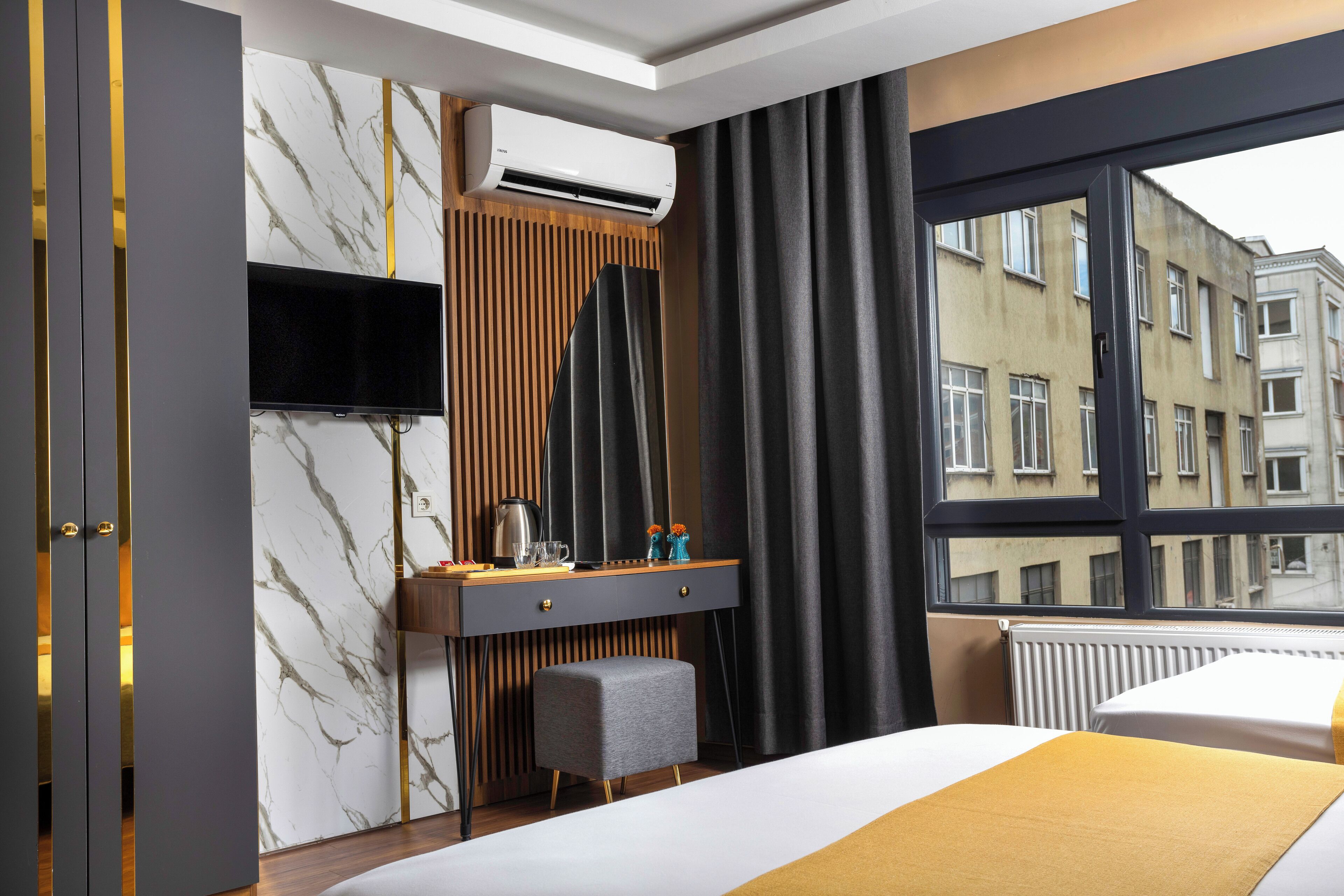 Habitación de hotel con cama, escritorio con televisor, aire acondicionado y ventana con vistas a edificios.