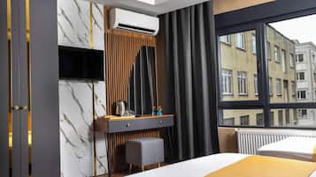 Habitación de hotel con cama, escritorio con televisor, aire acondicionado y ventana con vistas a edificios.