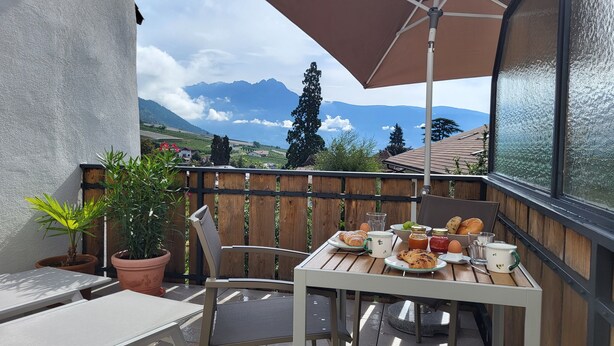 A balcony with a table set for breakfast, overlooking a mountainous landscape. - Fruemess Superior (Partschins)
