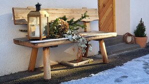 A wooden bench with a lantern and a potted plant against a white wall, next to a wooden door. - Fruemess Superior (Partschins)