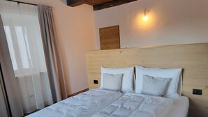 A large bed with a wooden headboard, white bedding, and a light fixture above it. - Fruemess Superior (Partschins)