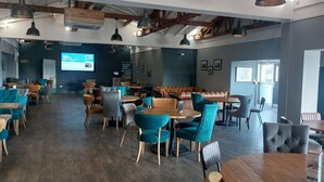 Ett rymligt café med träbord och stolar, en stor sittgrupp och en projektionsduk på väggen.