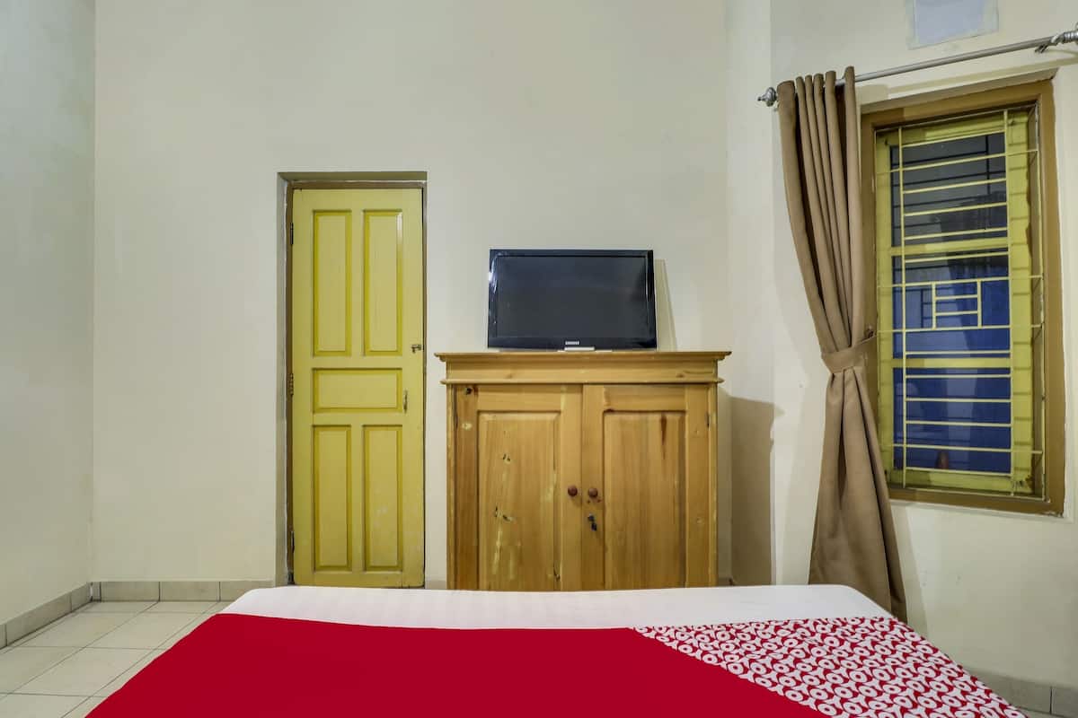 A room with a bed, a television on a wooden cabinet, a yellow door, and a window with curtains.