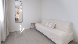 A minimalist living room with a beige sofa, a small wooden stool, and a wall-mounted mirror. - Hotel Tres Tocs (Ciutadella de Menorca)