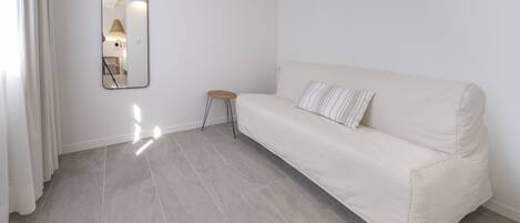 A minimalist room with a light-colored sofa, a small stool, and a wall-mounted mirror.