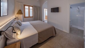 A bedroom with a bed, a TV, a window with curtains, and an air conditioning unit. - Hotel Tres Tocs (Ciutadella de Menorca)