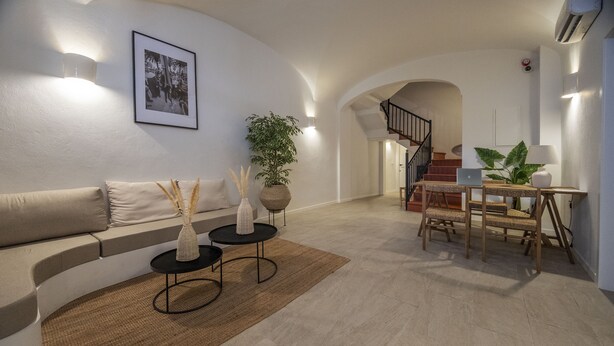 A modern living room with a curved sofa, a coffee table, a dining table with chairs, and a staircase leading to an upper floor. - Hotel Tres Tocs (Ciutadella de Menorca)