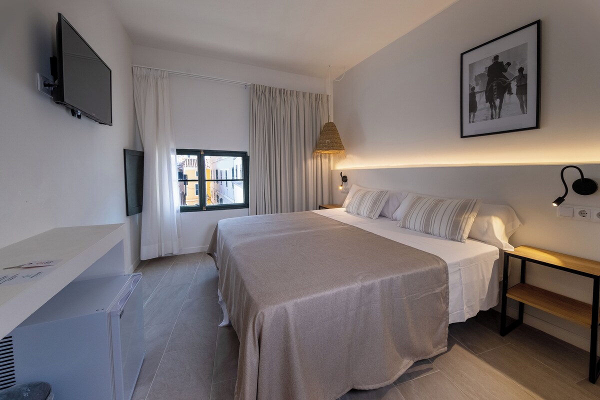 Un dormitorio con cama, mesita de noche, lámpara y un cuadro en la pared.