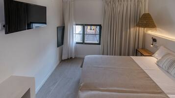 Une chambre d’hôtel avec un lit, un téléviseur fixé au mur, une fenêtre avec des rideaux et une lampe de chevet.