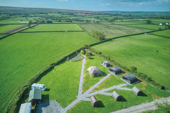 An aerial view of a rural property with green fields, a caravan, and several small buildings.
