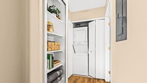 A laundry room with a white washing machine, shelves with folded towels, and a wooden floor.