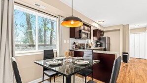 A modern kitchen with dark cabinets, a central island, and a dining area with a glass table and black chairs.