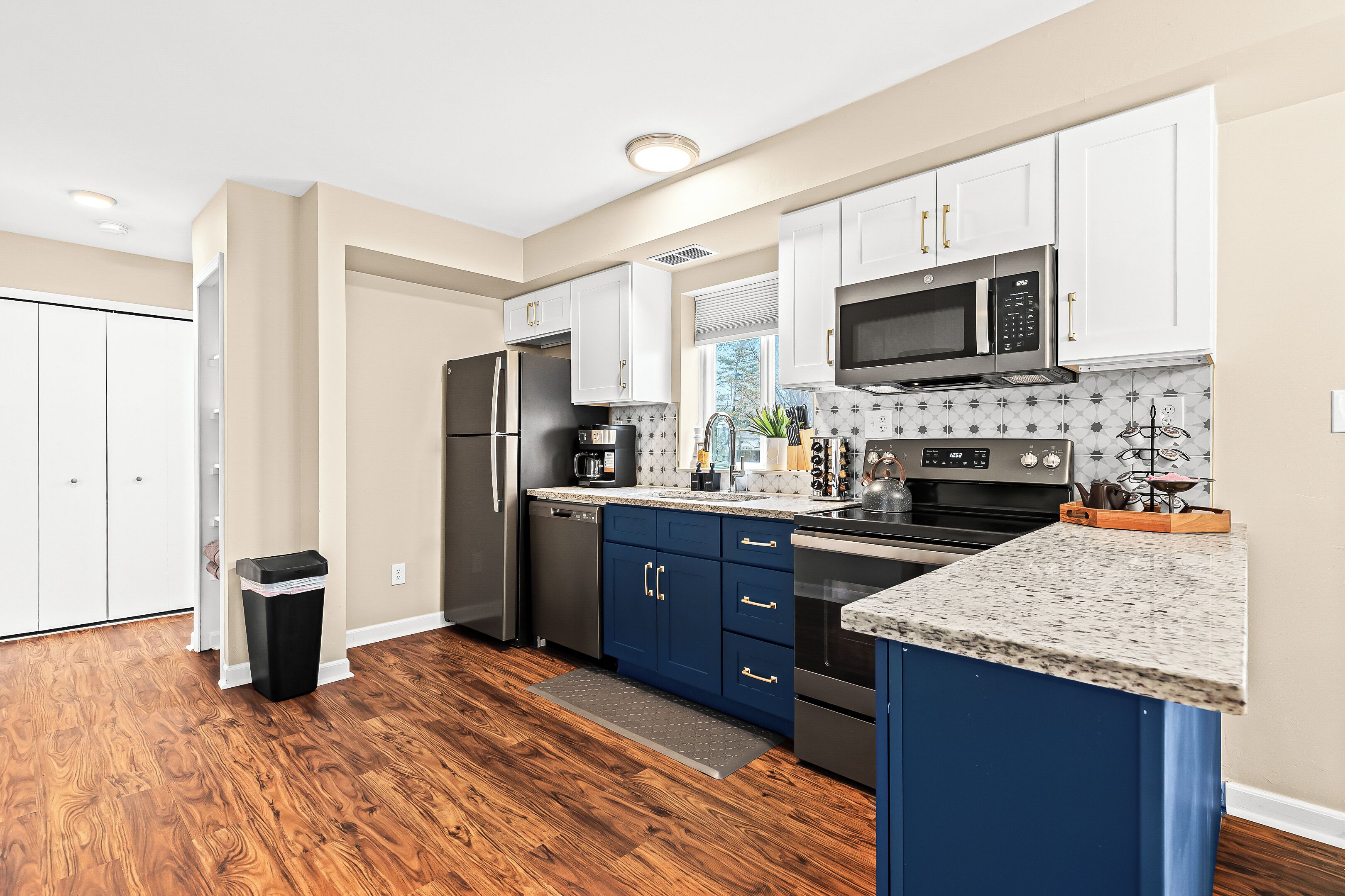 A modern kitchen with white and blue cabinets, stainless steel appliances, and a granite countertop.