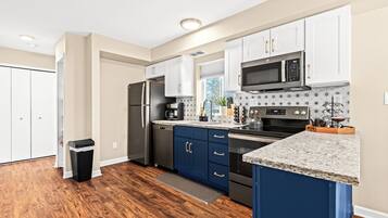 A modern kitchen with white and blue cabinets, stainless steel appliances, and a granite countertop.