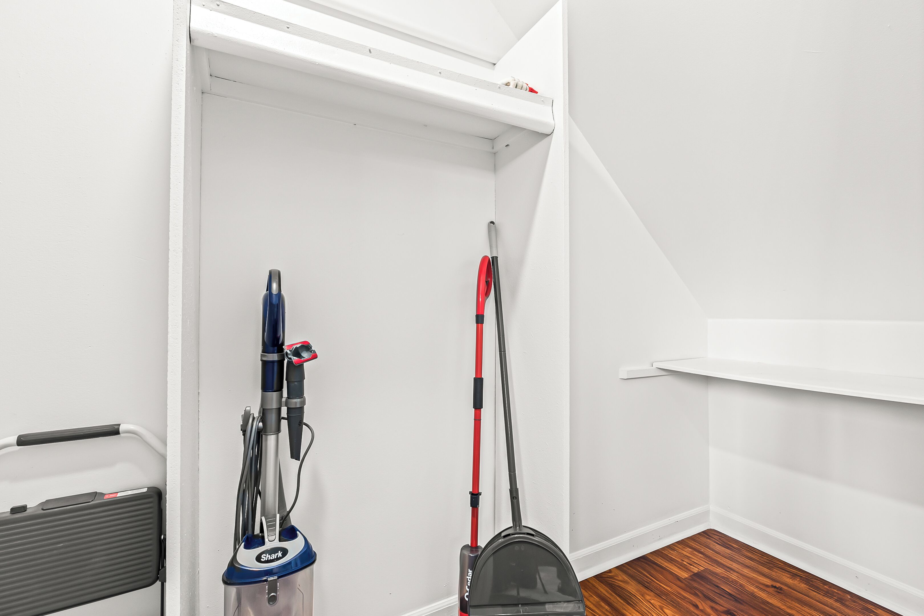 Een hoek van een kamer met een witte deur, een stofzuiger en een vloerreiniger die tegen de muur leunt.