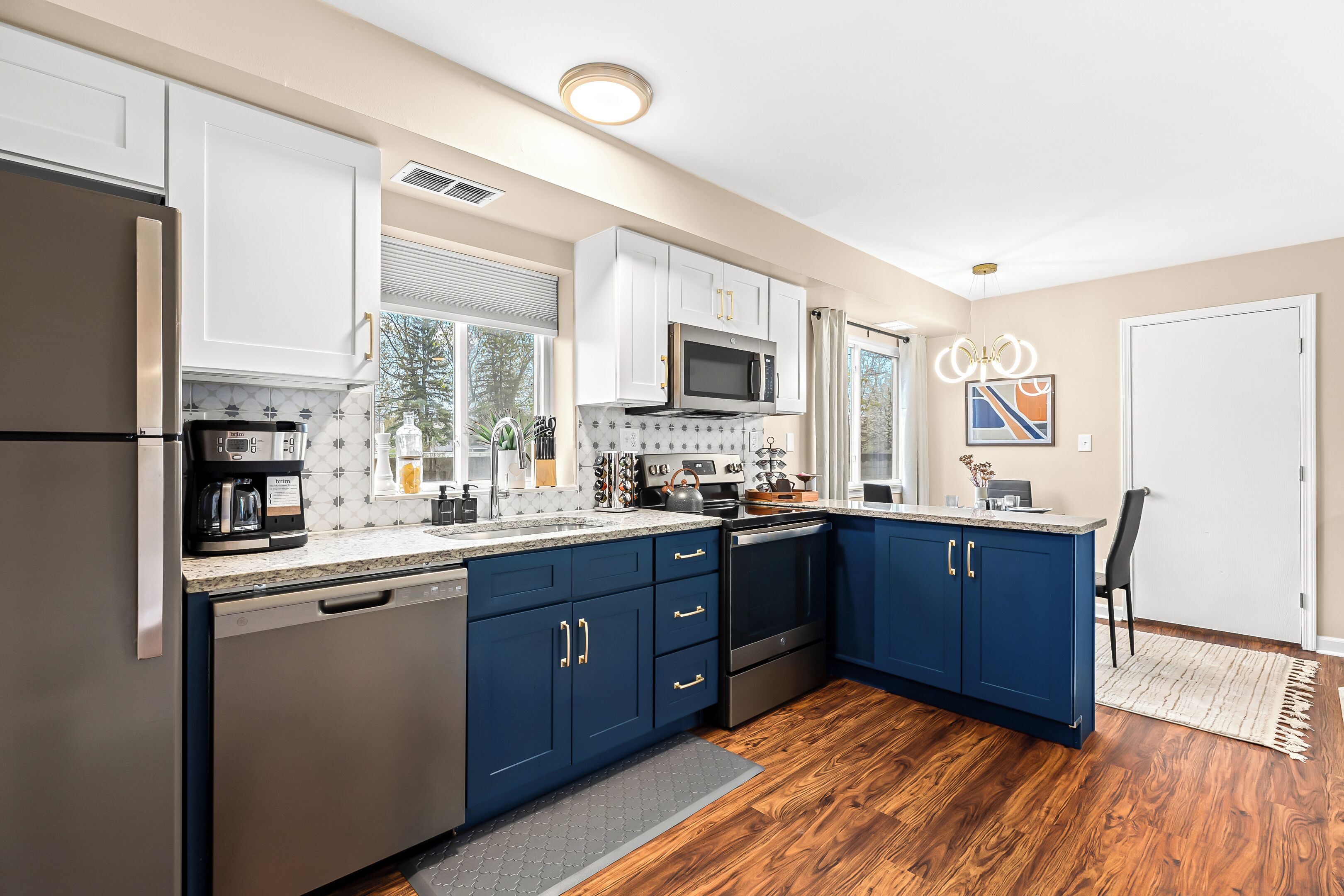 Una cocina moderna con gabinetes blancos y azules, electrodomésticos de acero inoxidable y piso de madera.
