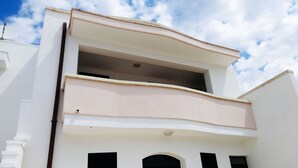 A two-story building with a flat roof, a balcony on the upper floor, and a door with a window on the lower floor.