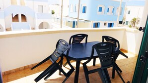 A balcony with a table and chairs, overlooking a blue and white building with arched windows.
