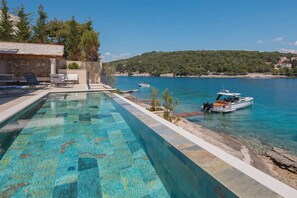 A swimming pool with clear water, lounge chairs, and a boat docked near the shore. - Stara in Selca With 4 Bedrooms and 4 Bathrooms (Selca)