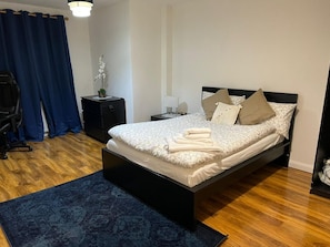 Relax in this serene bedroom with a large bed, neatly folded towels, and a side table with a lamp and plant.