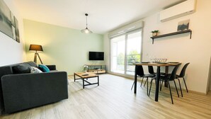 A modern living room with a sofa, coffee table, TV, and dining area with chairs and a table.