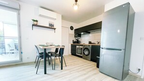 A modern kitchen with a built-in oven, washing machine, and refrigerator. There is a dining area with a table and chairs.