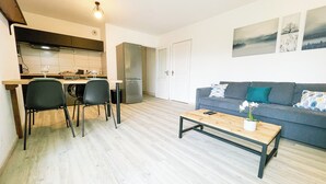 A modern living room with a grey sofa, a wooden coffee table, and a dining area with a table and chairs.