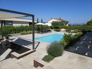 Uma área de piscina moderna ao ar livre, com pergolado, espreguiçadeiras e vista para o mar.