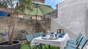 Un área de comedor al aire libre con una mesa preparada para cuatro, rodeada de sillas, una planta en maceta y una sombrilla.