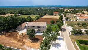 An aerial view of a residential area with a mix of houses and open fields, a paved road, and a clear sky. - Levlante in Kanfanar (Kanfanar)