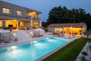 Una casa moderna de dos pisos con piscina, mobiliario de exterior y un jardín cuidado.