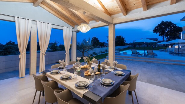 An outdoor dining area with a table set for four, surrounded by chairs, under a wooden pergola with a hanging light fixture. - Levlante in Kanfanar (Kanfanar)
