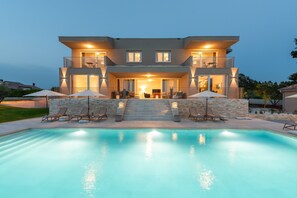 Una casa moderna de dos pisos con piscina, mobiliario exterior y una entrada bien iluminada.