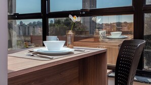 Un comedor con una mesa de madera, platos blancos, un jarrón transparente con una sola flor y una silla negra.