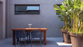 An outdoor patio area with a wooden table and chairs, a potted plant, and a string of lights.