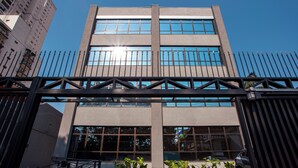 Un edificio moderno con un gran portón de entrada, plantas en macetas y un cielo azul despejado.